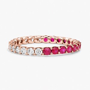 May include: A rose gold eternity band featuring a continuous row of alternating round-cut clear white diamonds and vibrant pink rubies set in a shared prong setting, creating a circular ring design with a polished metallic finish throughout.