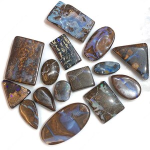 May include: A collection of polished boulder opals in various shapes including rectangles, ovals, and triangles. Each stone features a dark brown ironstone matrix with iridescent blue, green, and purple flashes of color throughout the surfaces.