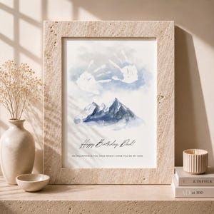 Könnte beinhalten: Ein gerahmter Druck mit einer Aquarell-Berglandschaft in Blau- und Weißtönen, mit zwei weißen Handabdrücken über den Gipfeln. Der Text lautet: Happy Birthday, Dad! NO MOUNTAIN IS TOO HIGH WHEN I HAVE YOU BY MY SIDE.