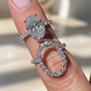 Peut inclure: Deux bagues en diamant. La bague supérieure présente un gros diamant de taille ovale avec un halo de petits diamants sur le bracelet. La deuxième bague est une forme ovale sertie de diamants. Les bagues sont sur un doigt avec du vernis à ongles rose.