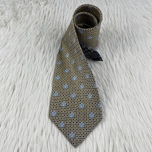 May include: A necktie featuring a dark brown and gold grid pattern with small, light blue, shield-shaped motifs distributed evenly across the fabric. The tie is rolled at the top, revealing a dark blue lining on the interior of the neckband.