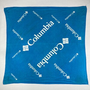 Op de afbeelding: Een vierkante, turquoise bandana met het witte Columbia-logo. De Columbia-tekst is diagonaal over de stof gedrukt, met het logo herhaald. De bandana is gemaakt van lichtgewicht materiaal.