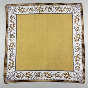 Peut inclure: Foulard carré jaune moutarde avec une bordure blanche ornée de motifs nautiques dorés et argentés. Le bord extérieur présente un motif pied-de-poule marron et blanc. Un accessoire élégant.