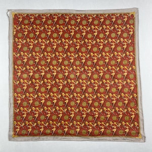 May include: A square scarf featuring a repeating pattern of gold coins, bows, and other decorative elements on a red background. The scarf has a light grey border with gold trim and the word "Burberrys" in the bottom right corner.