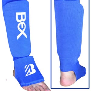 May include: Blue shin guards with white text that reads "BEX" and a stylized "B" on the ankle protector. The shin guards are made of a textured material and are designed to protect the lower leg.