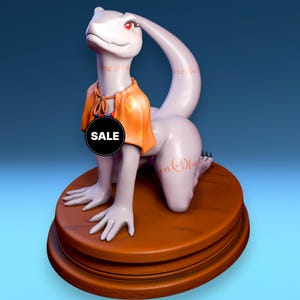 Può includere: Una statuetta a forma di lucertola viola chiaro con occhi rossi e abiti arancioni. La statuetta è inginocchiata su una base di legno marrone. Un cerchio nero con la scritta "SALE" è sul petto della statuetta.