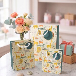 May include: Gift bags with a safari animal pattern, including giraffes, lions, and zebras. The bags have teal accents and white pom-pom handles. A vase of flowers and wrapped gifts are also in the image.