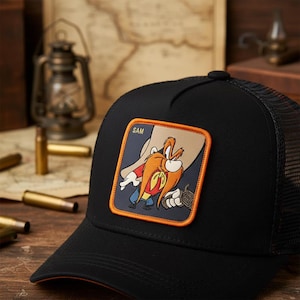 May include: Black trucker hat with a mesh back and a curved peak. The front features a square patch with a cartoon character illustration. The patch has the word "SAM" and an image of Yosemite Sam. A classic hat.