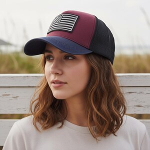 Op de afbeelding: Een bordeauxrode en marineblauwe baseballcap met een zwarte mesh achterkant. De pet heeft een wit en zwart Amerikaans vlagpatch. De klep is marineblauw.