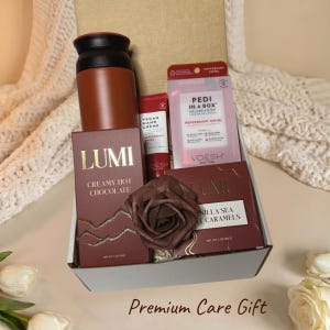 May include: A gift box containing a brown tumbler, a tube of peppermint swirl vegan hand creme, a Pedi in a Box kit, a box of Lumi creamy hot chocolate, a box of Lumi vanilla sea salt caramels, and a dark brown fabric rose decoration.