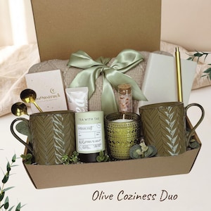 Può includere: Una confezione regalo contenente due tazze verde oliva testurizzate, un barattolo di tè Tea with Tae Moroccan Mint, un portacandele in vetro verde, una tavoletta di cioccolato Moonstruck, un flacone di sali da bagno rosa, un taccuino, una penna dorata e un nastro verde salvia.