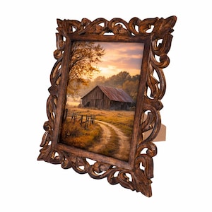 May include: A decorative wooden picture frame with an autumn landscape scene. The frame is a dark brown color with ornate, carved details. The picture shows a barn, dirt road, and fence in a field with a sunset.