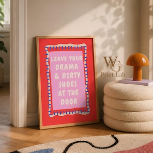 May include: A rectangular framed wall art print with a red background and a central pink rectangle featuring the white text: LEAVE YOUR DRAMA & DIRTY SHOES AT THE DOOR. The pink area is bordered by a cream-colored scalloped edge with blue stitching.