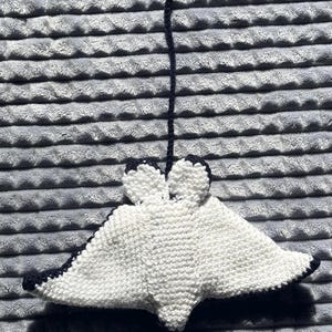 K&ouml;nnte beinhalten: Handgefertigter, wei&szlig;-blauer Strickrochen-Ornament. Der Rochen hat einen flachen, rautenf&ouml;rmigen K&ouml;rper mit abgerundeten Kanten und einem langen, d&uuml;nnen Schwanz. Die Kanten und der Schwanz sind marineblau, der K&ouml;rper ist wei&szlig;. Das Ornament wird von einer marineblauen Schnur gehalten.