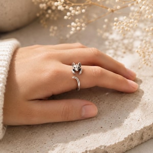 Peut inclure: Une bague ouverte de couleur argentée représentant une petite souris sculptée. La tête de la souris est située à une extrémité de l'anneau, tandis que l'autre extrémité se courbe pour ressembler à une queue, créant un effet d'enroulement.