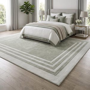 Puede incluir: Una alfombra rectangular grande con un panel central de color verde salvia s&oacute;lido, enmarcado por m&uacute;ltiples bordes conc&eacute;ntricos en varios tonos de gris claro y verde salvia, creando un efecto geom&eacute;trico superpuesto.