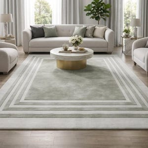 Puede incluir: Una alfombra rectangular grande que presenta un panel central de color verde salvia suave enmarcado por m&uacute;ltiples bordes conc&eacute;ntricos en varios tonos de gris claro y blanco, creando un efecto geom&eacute;trico en capas sobre el suelo.