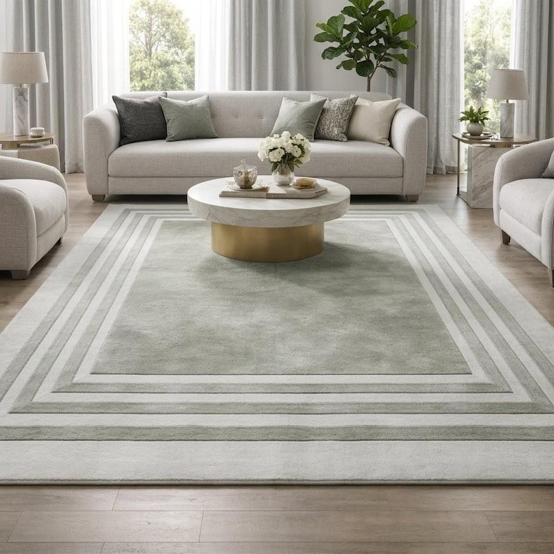 Puede incluir: Una alfombra rectangular grande que presenta un panel central de color verde salvia suave enmarcado por m&uacute;ltiples bordes conc&eacute;ntricos en varios tonos de gris claro y blanco, creando un efecto geom&eacute;trico en capas sobre el suelo.