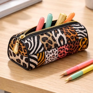 Könnte beinhalten: Rechteckiges Federmäppchen mit einem Patchwork-Design aus Tiermustern, darunter Leoparden- und Zebramuster. Das Etui ist offen und zeigt bunte Marker. Ein goldener Reißverschluss und ein Zipper vervollständigen das Design. Zwei rosa und gelbe Stifte liegen auf dem Tisch.