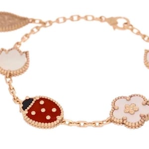 May include: A gold-toned bracelet featuring a ladybug, flower, and leaf charm design. The bracelet includes a chain with a lobster clasp. The ladybug charm is red with black spots, and the flower and leaf charms are white.