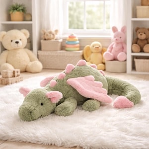 May include: A soft green dragon toy with pink wings and ear details rests on a white fluffy rug. The dragon is surrounded by other soft toys, including teddy bears and a pink rabbit, in a bright, inviting room.