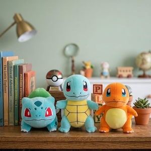 May include: Three plush Pokémon figures: Bulbasaur, Squirtle, and Charmander, are displayed on a wooden surface. Bulbasaur is green and blue, Squirtle is blue and yellow, and Charmander is orange. A Poké Ball and books are in the background.