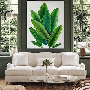 May include: A large, framed canvas art piece featuring a detailed depiction of lush, green tropical leaves. The artwork is mounted on a white background and hangs above a cream-colored sofa. The room has large windows and a modern aesthetic.