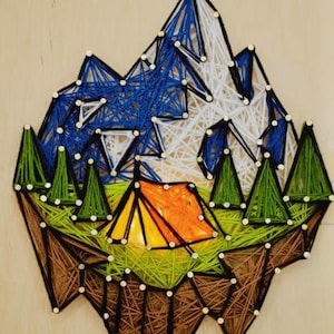 May include: String art landscape featuring a mountain range with blue and white peaks, green trees, and an orange tent. The artwork is crafted with string and nails on a wooden background, evoking a camping theme.