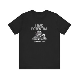 May include: Black t-shirt with a graphic design featuring a skeleton slumped against a stack of books. The text "I HAD POTENTIAL" is above the illustration, with "(KEY WORD: HAD)" below.