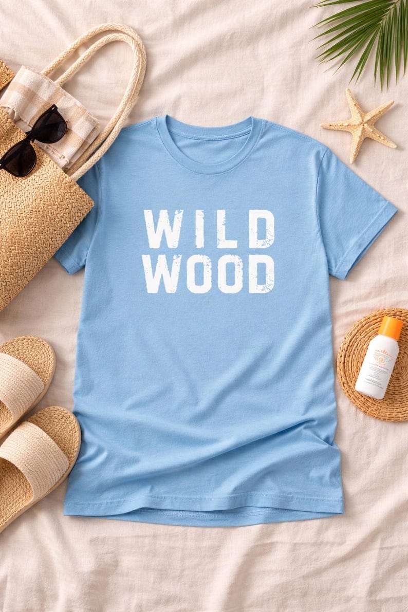 K&ouml;nnte beinhalten: Hellblaues T-Shirt mit dem wei&szlig;en Aufdruck "WILD WOOD". Das Bild zeigt Strandaccessoires: eine Strohtasche, Sonnenbrille, Sandalen und Sonnencreme. Ein Seestern und ein Palmblatt erg&auml;nzen das Strandthema und vermitteln Urlaubsstimmung.