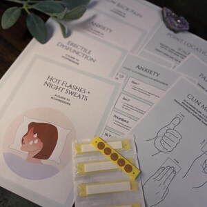 May include: A collection of printed guides on topics like erectile dysfunction, anxiety, and acupressure for hot flashes and night sweats. A yellow strip with brown circular pads is in the foreground, along with a drawing of a person on a pillow.
