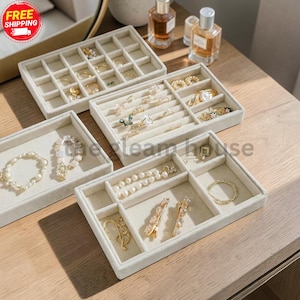 May include: A set of four beige velvet jewelry organizer trays with various compartments for rings, bracelets, and earrings. The trays are arranged to display assorted gold and pearl jewelry pieces, including necklaces, hair clips, and rings.