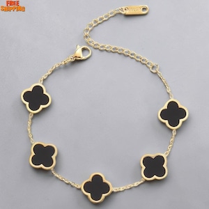 May include: Gold-tone bracelet featuring five black clover-shaped charms. The bracelet has a delicate chain design and a lobster clasp closure. The charms are outlined in gold, creating a striking contrast against the black enamel.