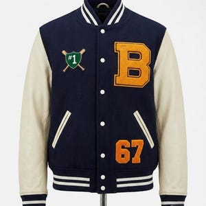 Może przedstawiać: Granatowa kurtka w stylu college z kremowymi rękawami. Posiada dużą pomarańczową naszywkę z literą "B", numer "67" i zielony emblemat baseballowy. Kurtka ma białe paski na kołnierzu, mankietach i obszyciu oraz zapięcie na guziki.