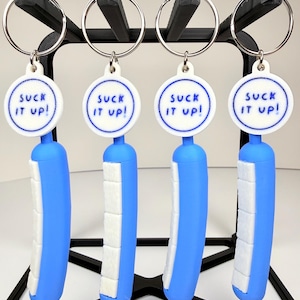 May include: Four keychains with a blue and white design. Each keychain has a blue cylindrical body with white rectangular accents and a circular tag with the text "SUCK IT UP!". The keychains are attached to silver key rings.