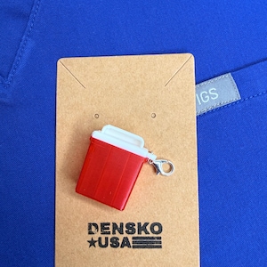 May include: A red and white miniature sharps container charm with a silver clasp is displayed on a brown card. The card has the text "DENSKO USA" printed on it. The background is a solid royal blue fabric.