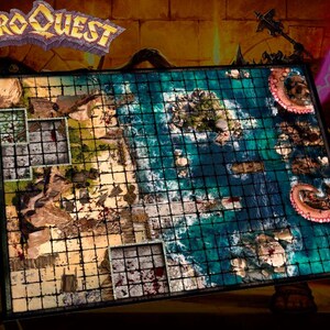 Peut inclure: Un plateau de jeu détaillé avec un motif quadrillé, représentant des zones terrestres et maritimes. Le plateau a un design de type carte avec le texte "HEROQUEST" en haut. La zone maritime a un code couleur bleu et vert, et les zones terrestres sont marron.
