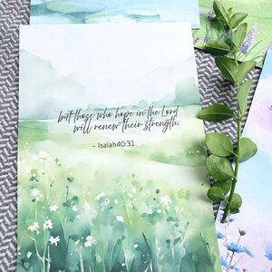 May include: A rectangular art print featuring a watercolor landscape of green rolling hills and white wildflowers. The text reads, but those who hope in the Lord will renew their strength. - Isaiah 40:31. The print is displayed with a green leafy stem.