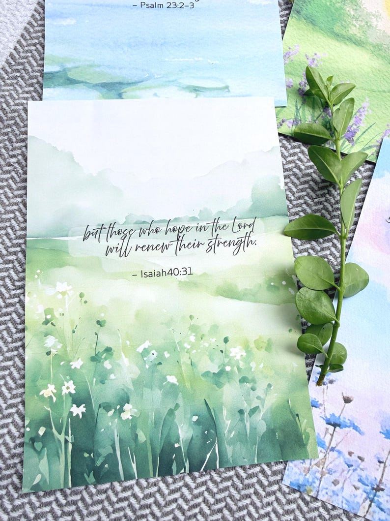 May include: A rectangular art print featuring a watercolor landscape of green rolling hills and white wildflowers. The text reads, but those who hope in the Lord will renew their strength. - Isaiah 40:31. The print is displayed with a green leafy stem.