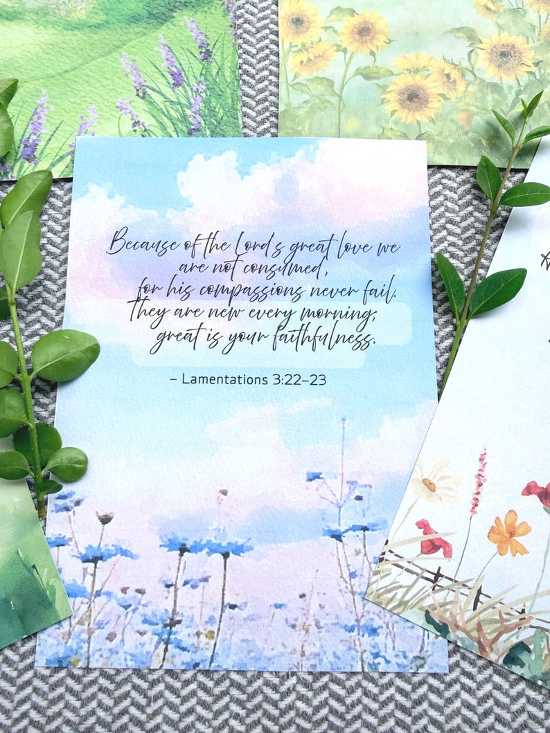 May include: A rectangular card featuring a watercolor sky background with blue and white clouds above a field of blue flowers. The text reads: Because of the Lord's great love we are not consumed, for his compassions never fail. They are new every morning, great is your faithfulness. - Lamentations 3:22-23.