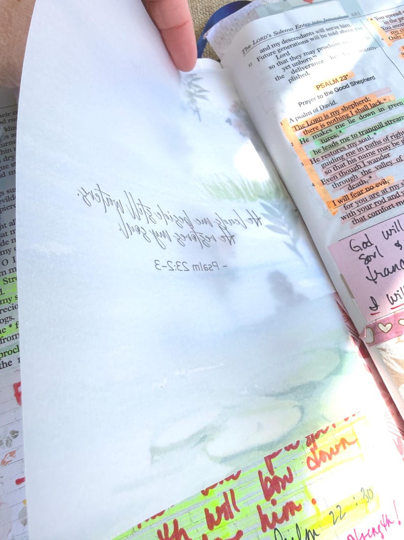 May include: Open Bible with handwritten notes and highlighted passages. The text includes Psalm 23 and other biblical verses. Colorful sticky notes and underlining highlight key phrases. The page is held open by a hand.