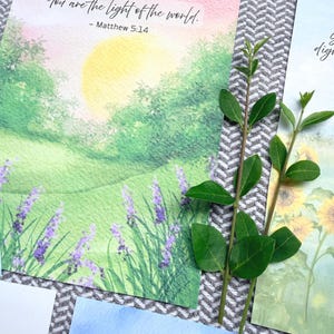 May include: A rectangular art print featuring a watercolor landscape of a green field, purple lavender flowers, and a yellow sun, with the text "You are the light of the world. - Matthew 5:14" printed in black ink at the top of the paper.