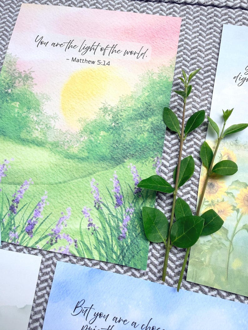 May include: A rectangular art print featuring a watercolor landscape of a green field, purple lavender flowers, and a yellow sun, with the text "You are the light of the world. - Matthew 5:14" printed in black ink at the top of the paper.