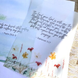 May include: Two watercolor bookmarks with floral designs and scriptural text. One bookmark features a field of flowers with the text "Psalm 23:2-3". The other bookmark has the text "Zephaniah 3:17". The bookmarks are on a neutral background.