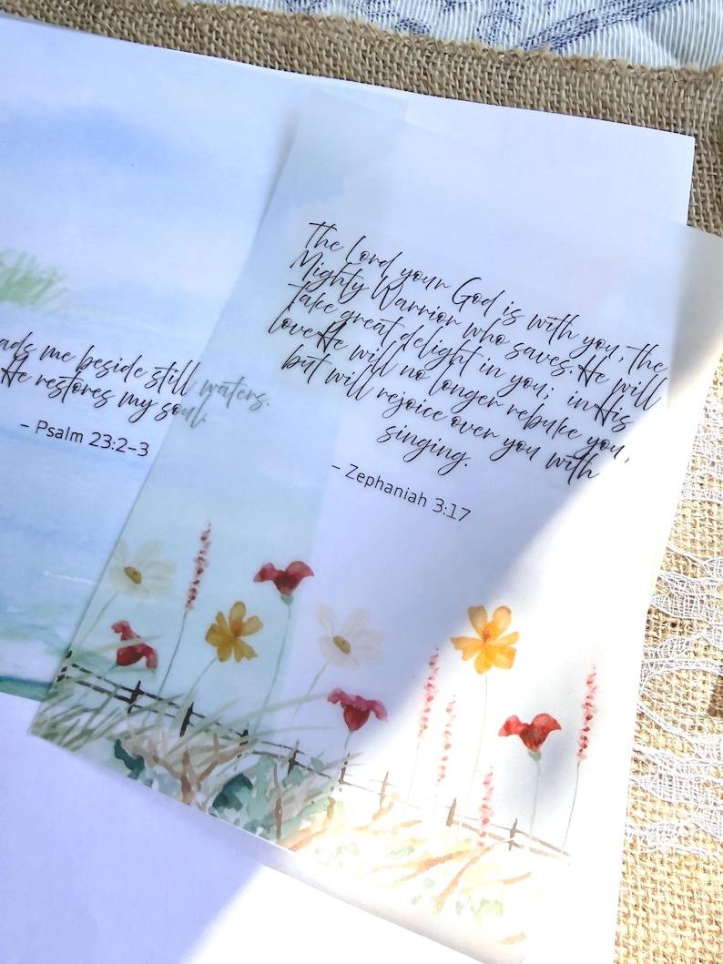 May include: Two watercolor bookmarks with floral designs and scriptural text. One bookmark features a field of flowers with the text "Psalm 23:2-3". The other bookmark has the text "Zephaniah 3:17". The bookmarks are on a neutral background.