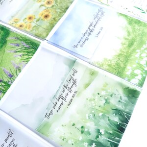 May include: A collection of watercolor art cards featuring nature scenes and inspirational quotes. The cards display images of sunflowers, lavender, and fields with text from the Bible. The cards are in a variety of colors, including green, yellow, and purple.