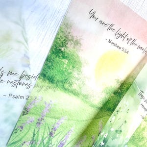May include: Close-up of three watercolor-style bookmarks with inspirational quotes. One bookmark reads "You are the light of the world" from Matthew 5:14. Another says "He leads me beside still waters" from Psalm 23:2-3. The third bookmark has the text "Those who renew" from Isaiah.