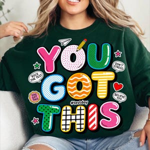May include: Dark green sweatshirt with the words "YOU GOT THIS" in colorful, bubble-style letters. Additional text includes "Rock the Test", "Don't Stress", and "Believe You". The sweatshirt has a playful, encouraging design.