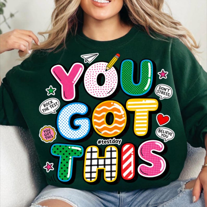 May include: Dark green sweatshirt with the words "YOU GOT THIS" in colorful, bubble-style letters. Additional text includes "Rock the Test", "Don't Stress", and "Believe You". The sweatshirt has a playful, encouraging design.