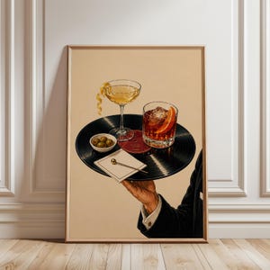 May include: A framed art print featuring a black vinyl record used as a serving tray. On the record sits a stemmed cocktail glass with a lemon twist, a rocks glass with an orange slice and ice, a small bowl of green olives, and a cocktail pick.